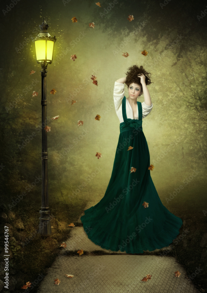 Young girl in long dress in the autumn park spellbound is looking at the sparkling lantern