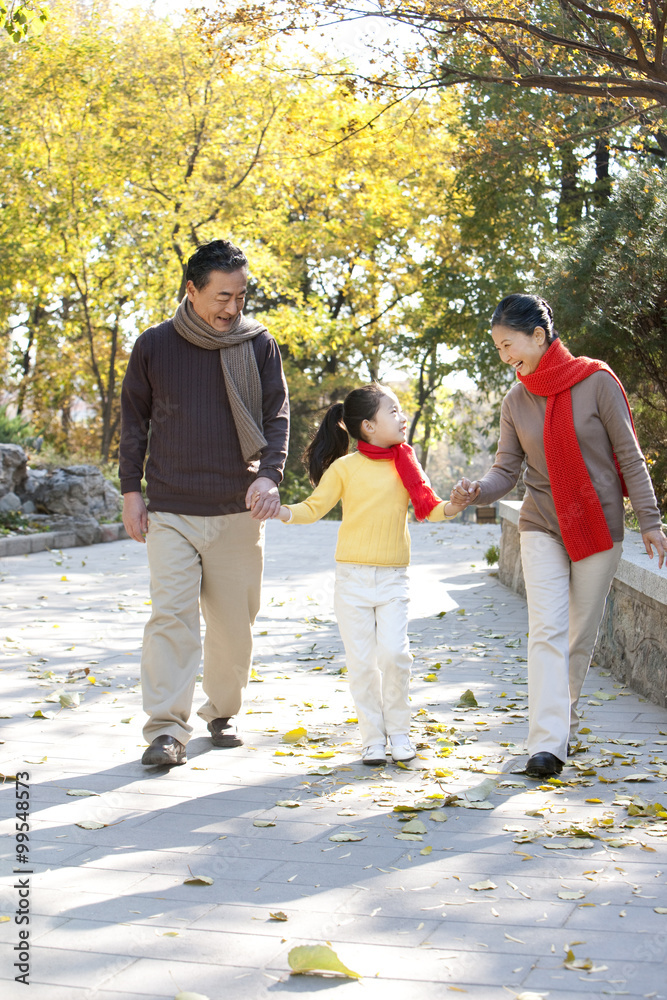 Fototapeta premium Senior couple with granddaughter strolling through the park in Autumn