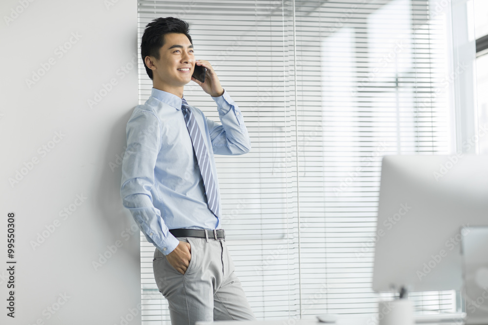 Young businessman talking on cell phone in office Young businessman talking on cell phone in office