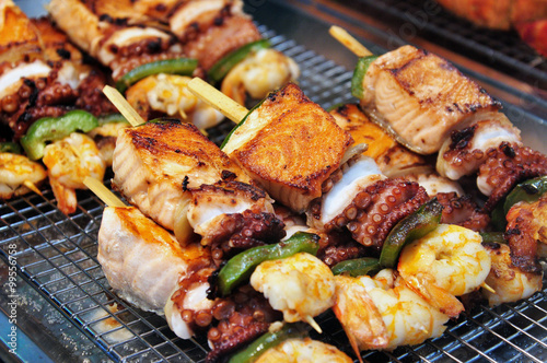Photography Grilled skewers of seafood consist of salmon, cuttlefish, scampi, and vegetables