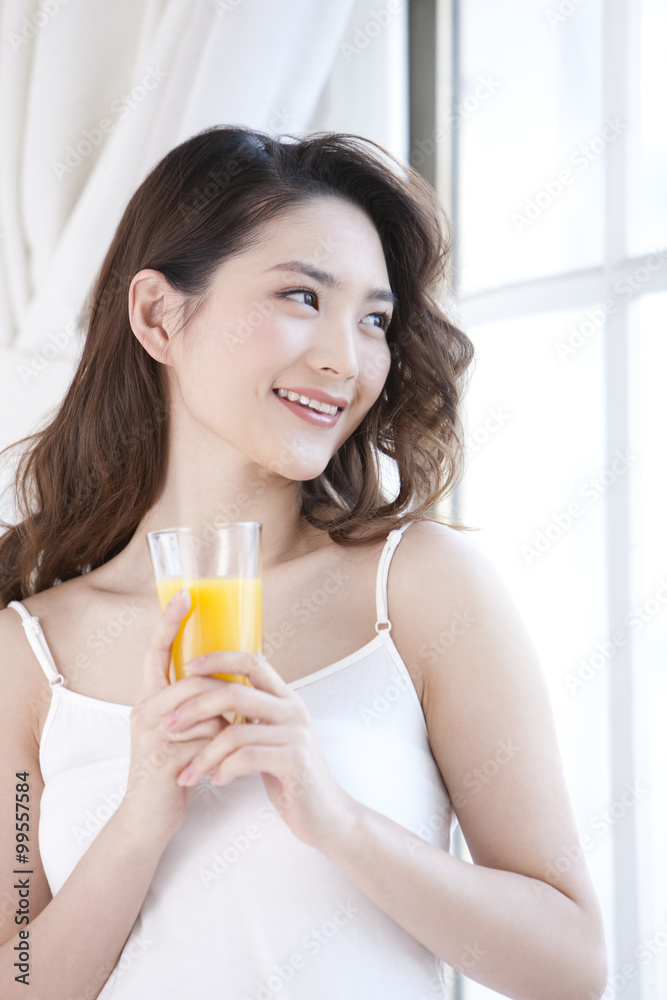 Young woman drinking orange juice by window Young woman drinking orange juice by window
