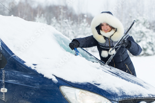Beautiful young woman removing snow from her car.