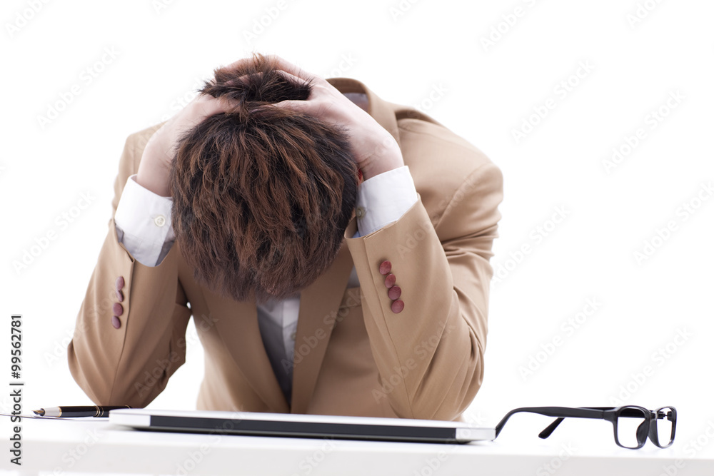Frustrated businessman with head in hands at office desk
