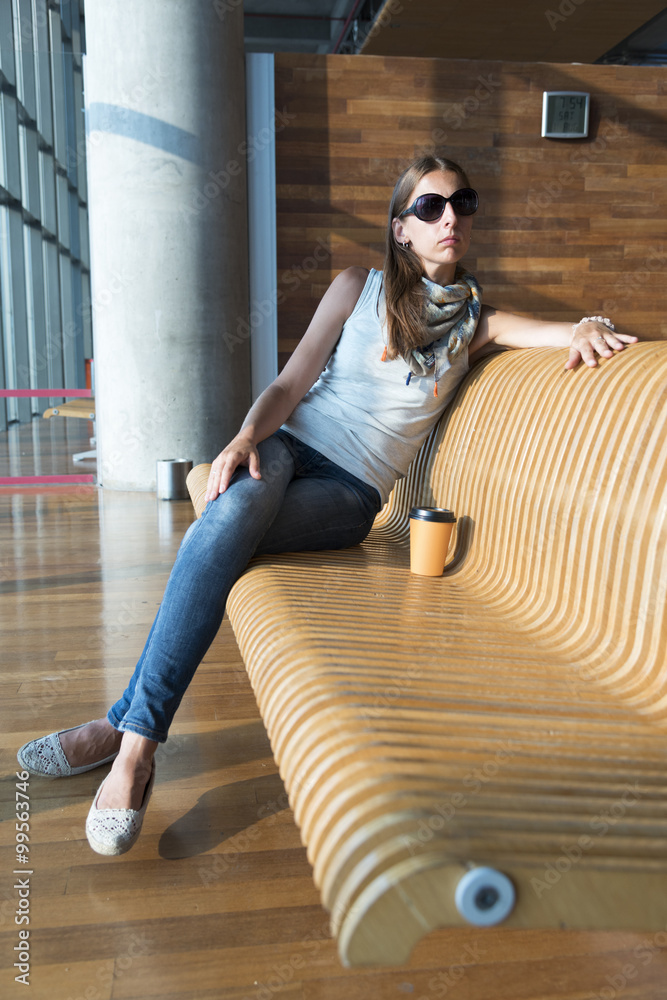 Woman in sunglasses, with paper cup, sitting on the wooden bench