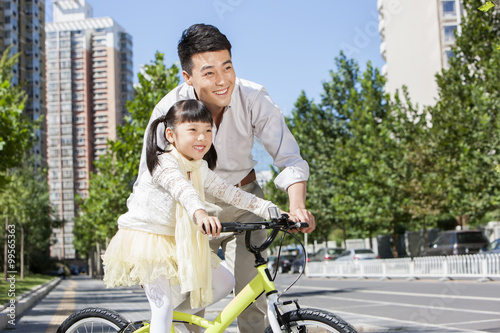 Fototapeta Naklejka Na Ścianę i Meble -  Kindly young father teaching daughter riding a bike on street
