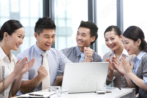 Businesspeople cheering while looking over a laptop