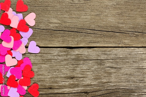 Colorful paper Valentines Day hearts forming a side border against rustic wood