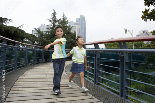 Young Boy And Young Girl Running Across A Bridge In A Park © Blue Jean Images
