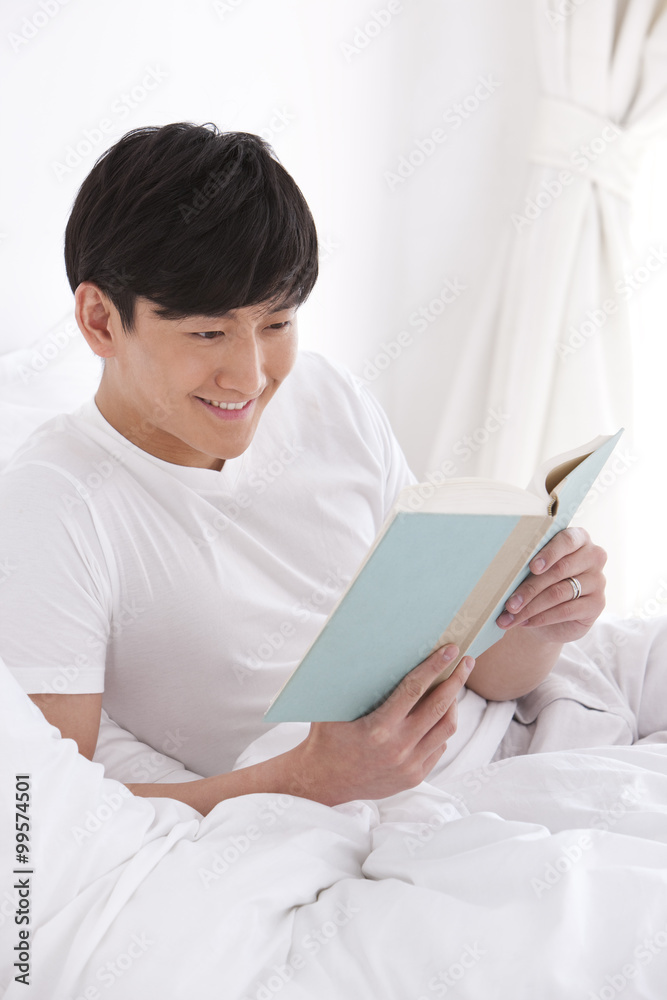 Young man reading a book in bed Young man reading a book in bed
