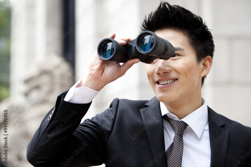Smiling young businessman looking through binoculars outdoors, Hong Kong Smiling young businessman looking through binoculars outdoors, Hong Kong