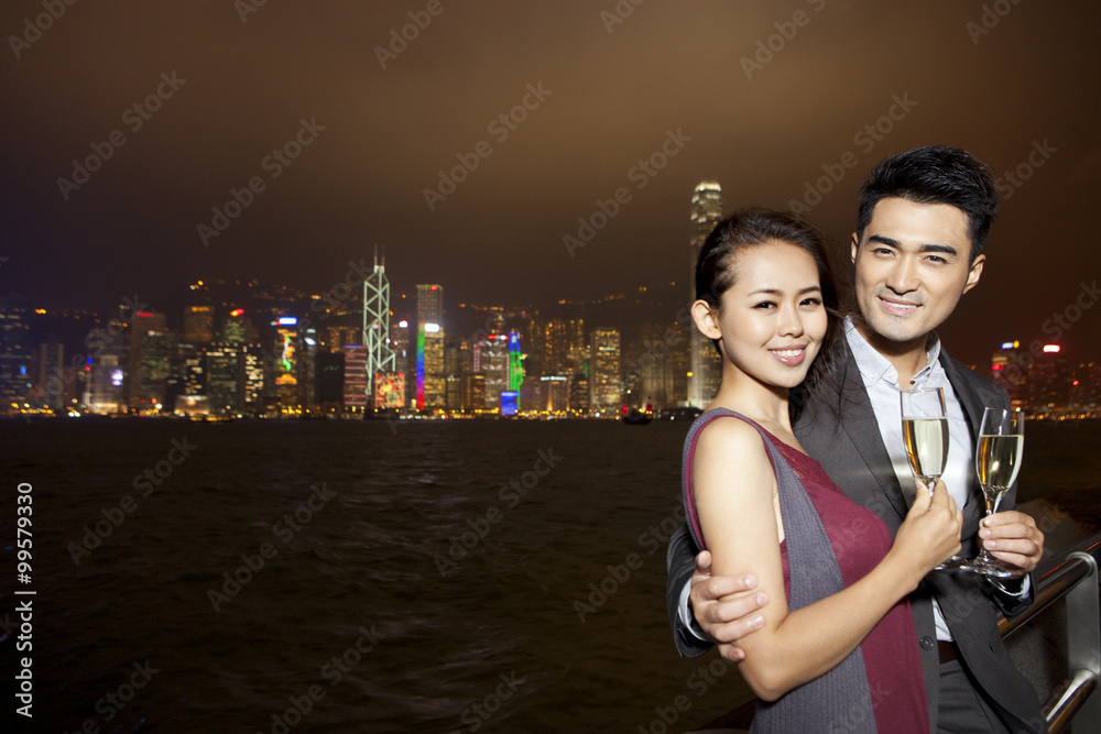Fototapeta premium Happy young couple enjoying the night view of Victoria Harbor with champagne, Hong Kong