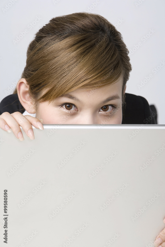 Young businesswoman peeking from laptop behind Young businesswoman peeking from laptop behind