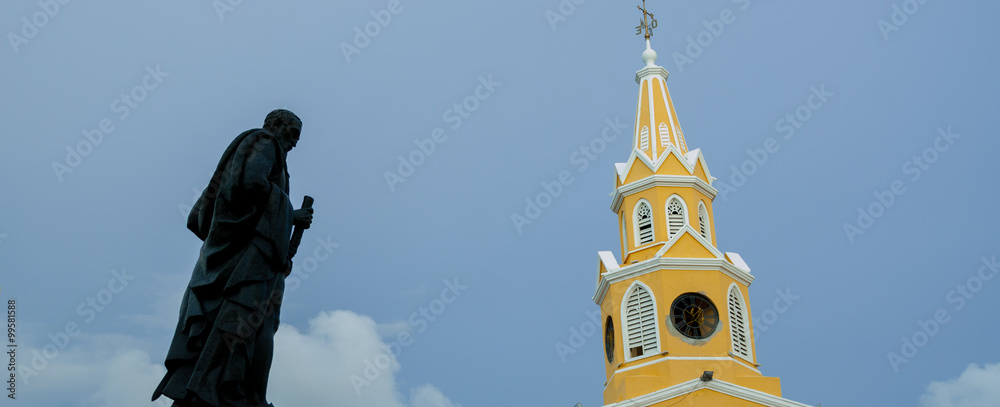 Black statue and yellow clock tower in front of a blue sky Black statue and yellow clock tower in front of a blue sky