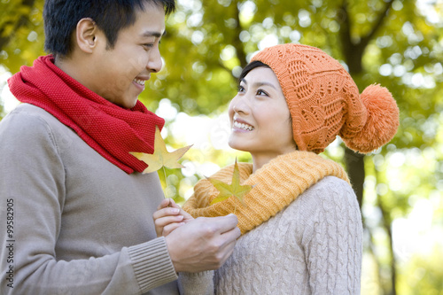 Young Couple in a Park in Autumn Holding Golden Maple Leaves