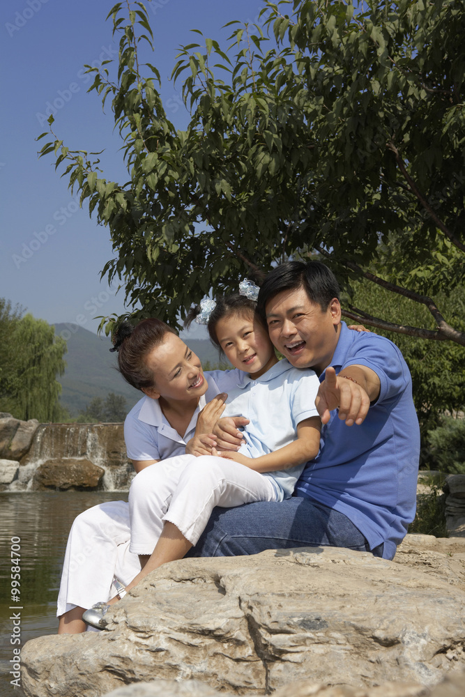 Girl And Parents Sitting On Rock, Arms Around Each Other Girl And Parents Sitting On Rock, Arms Around Each Other