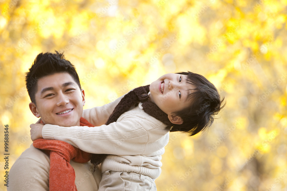 Father carrying son surrounded by Autumn trees in the background Father carrying son surrounded by Autumn trees in the background