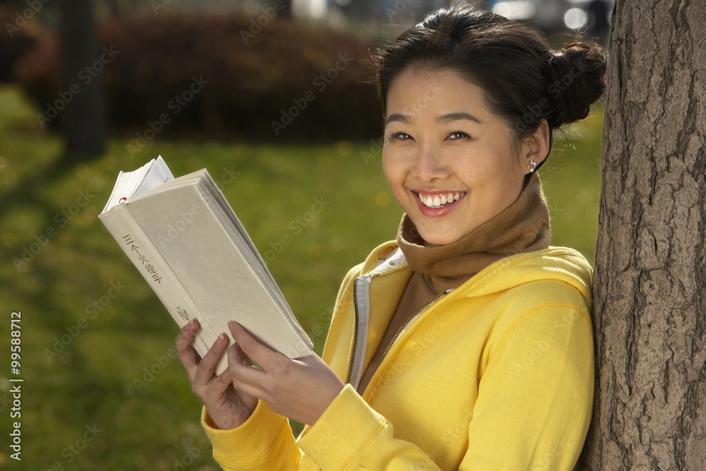 Young Woman Leaning Against A Tree Reading Her Book Young Woman Leaning Against A Tree Reading Her Book