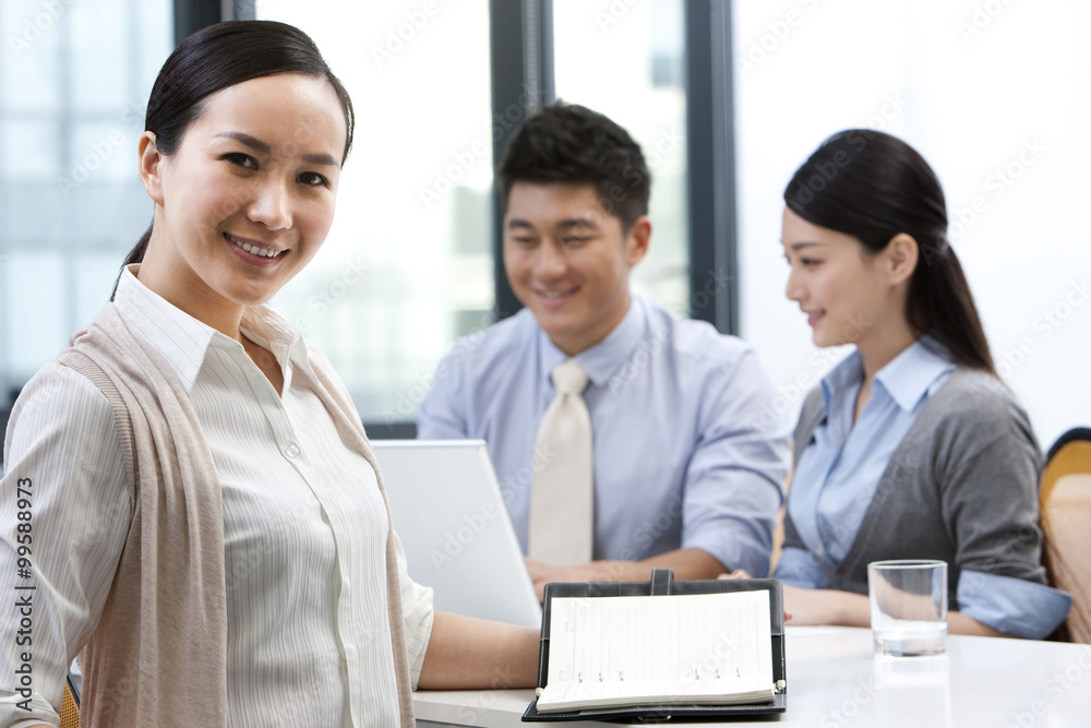 Businesswoman sitting with colleagues in the background Businesswoman sitting with colleagues in the background