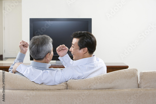 Father and adult son playing rock, scissors, paper in front of widescreen television