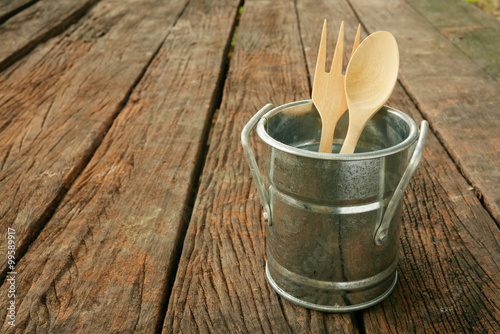 The small vintage zinc pot with wooden spoon and fork on the old dark brown wooden planks.