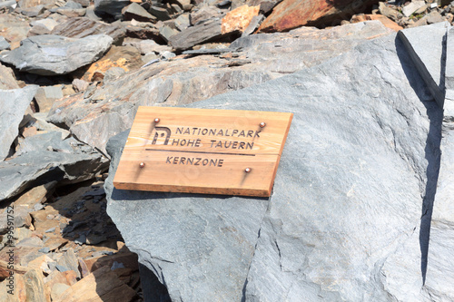 Wooden sign with German text "National park Hohe Tauern - Central zone" on a rock in the Alps, Austria