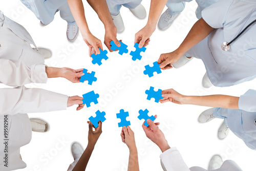 Medical Team Holding Blue Jigsaw Pieces In Huddle