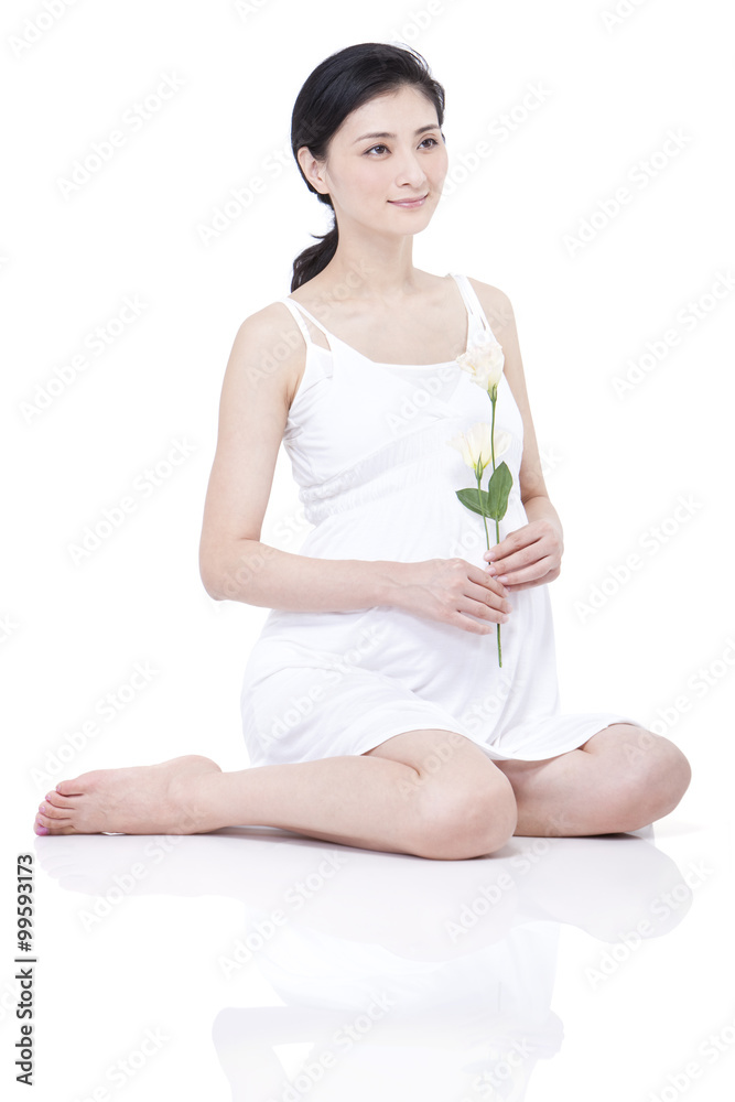 Young pregnant woman sitting cross-legged with carnation in hand Young pregnant woman sitting cross-legged with carnation in hand