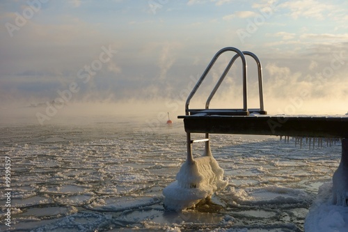 Ice covered swimming jetty and buoy in the freezing Baltic Sea in Helsinki, Finland just hours before complete freeze over of the sea on an extremely cold January morning (-20C) on 6 January 2016.  photo