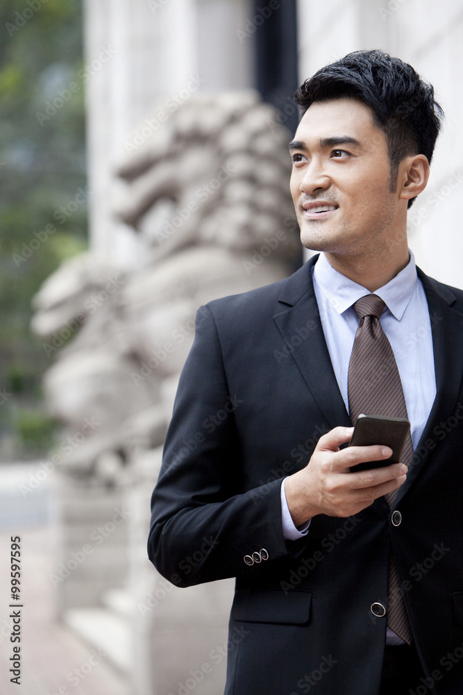 Confident businessman with smart phone looking at view, Hong Kong Confident businessman with smart phone looking at view, Hong Kong