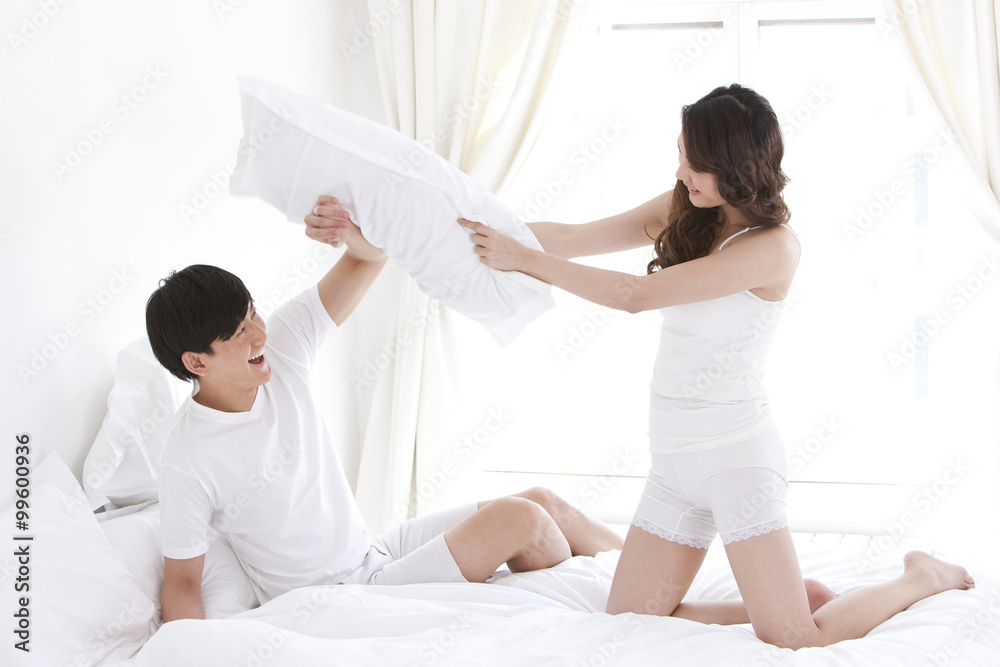 Fototapeta premium Young couple pillow-fighting in bed