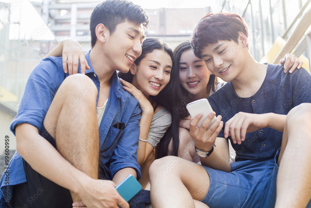 Young friends using smartphone while sitting outdoors Young friends using smartphone while sitting outdoors