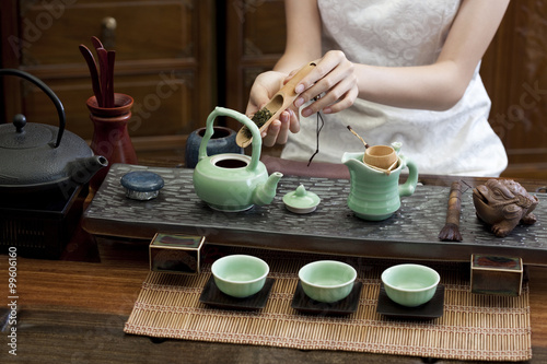 Young woman putting tea leaves into teapot