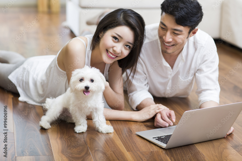 Young couple lying on floor using laptop with a cute dog Young couple lying on floor using laptop with a cute dog