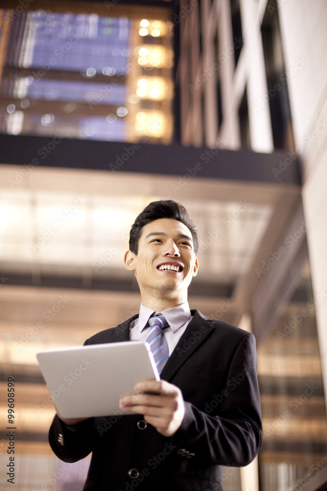 Fototapeta premium A businessman using a digital tablet outside an office building at night