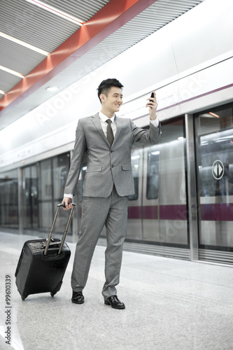 Young businessman on the phone while holding luggage on subway platform
