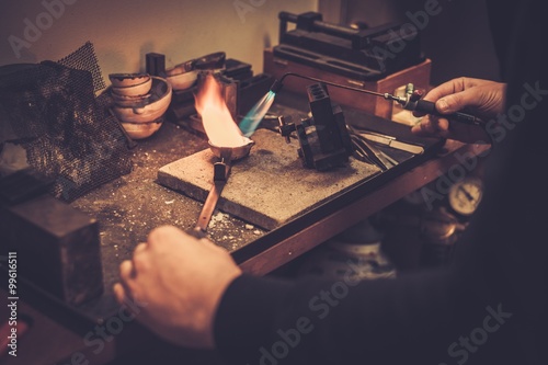 Goldsmith melting gold to liquid state in crucible with gasoline burner.