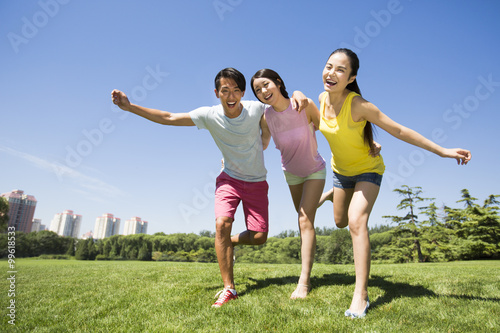 Three cheerful young adults standing arm in arm on grass