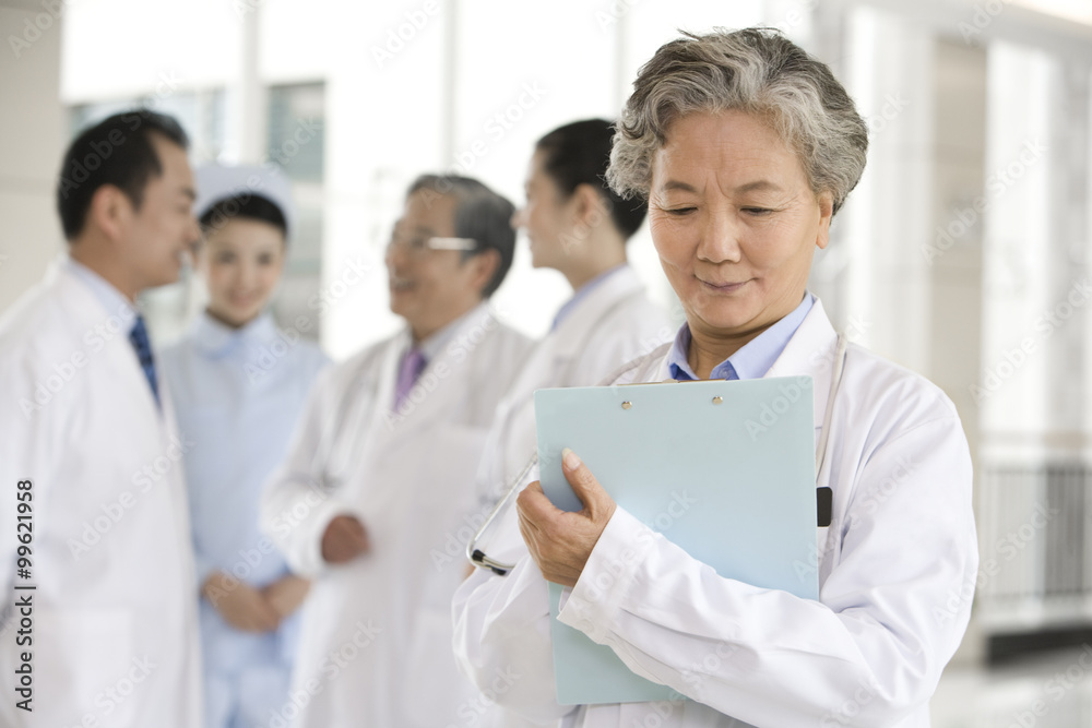 Senior Doctor in Forground with Clipboard, Doctors and a Nurse in Background