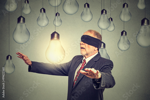 Blindfolded senior man walking through light bulbs searching for bright idea