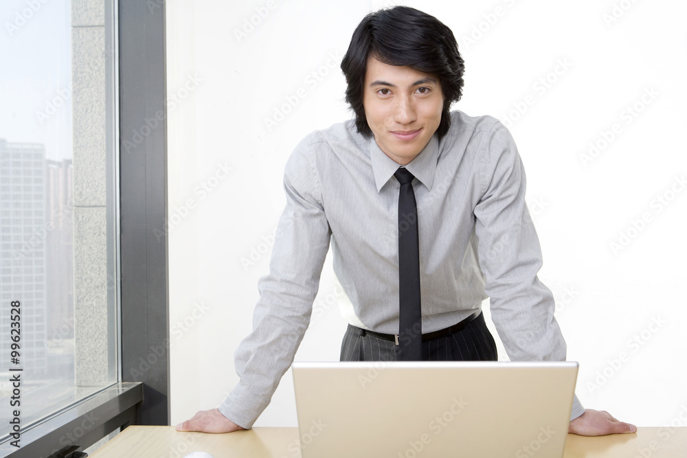 Young businessman leans on desk in front of laptop. Young businessman leans on desk in front of laptop.
