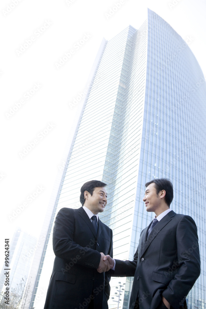 Businessmen shaking hands in front of tall building Businessmen shaking hands in front of tall building