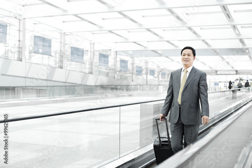 Mature businessman with wheeled luggage on airport escalator
