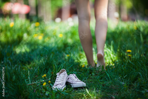 Woman walking barefoot on the grass, pink shoes in focus, shallow DOF photo