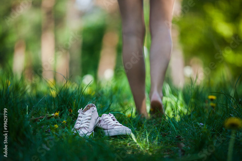 Woman walking barefoot on the green grass, shoes in focus, shallow DOF