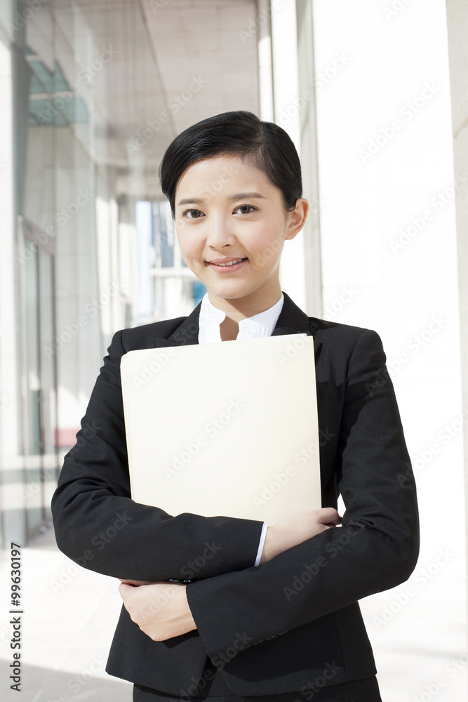 Smiling young businesswoman with a folder in downtown district Smiling young businesswoman with a folder in downtown district