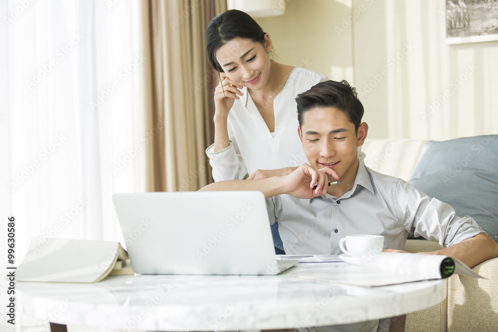 Young man working at home while his wife looking at him Young man working at home while his wife looking at him