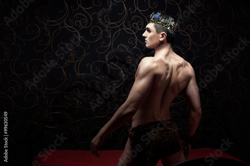 Canvas Print Handsome man wearing crown standing on a bed.