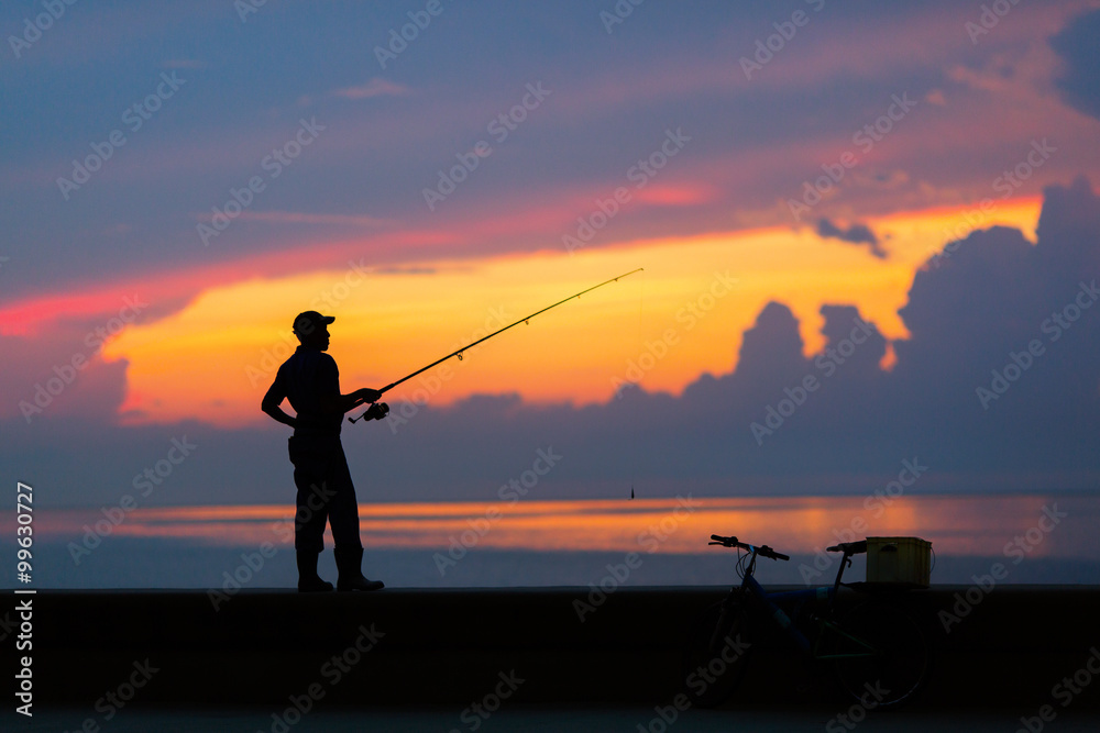 Fisherman silhouette on the beach at colorful sunset.