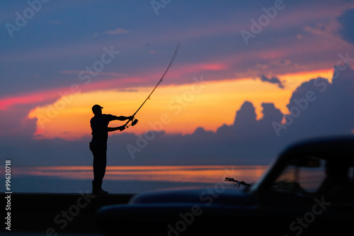 Fisherman silhouette on the beach at colorful sunset.