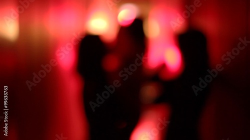 Silhouette of three sexy women dancing in a blurry, red corridor with her hands raised. Medium shot.
